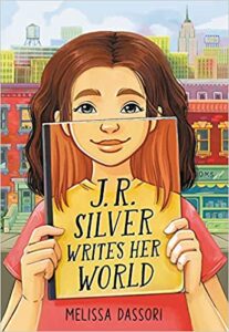 J. R. Silver Writers Her World by Melissa Dassori cover shows a girl holding up a book in front of the lower half of her face. The cover of the book she's holding completes the image of her face.