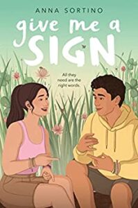 Give Me a Sign by Anna Sortino cover shows a girl on the left in a tank top and shorts with her hands one on top of the other with her index finger and thumb extended. Sitting next to her is a boy in a hoodie and shorts with his hands in front of his body, his index finger and pinky extended. Tall grass and flowers in the background behind them.